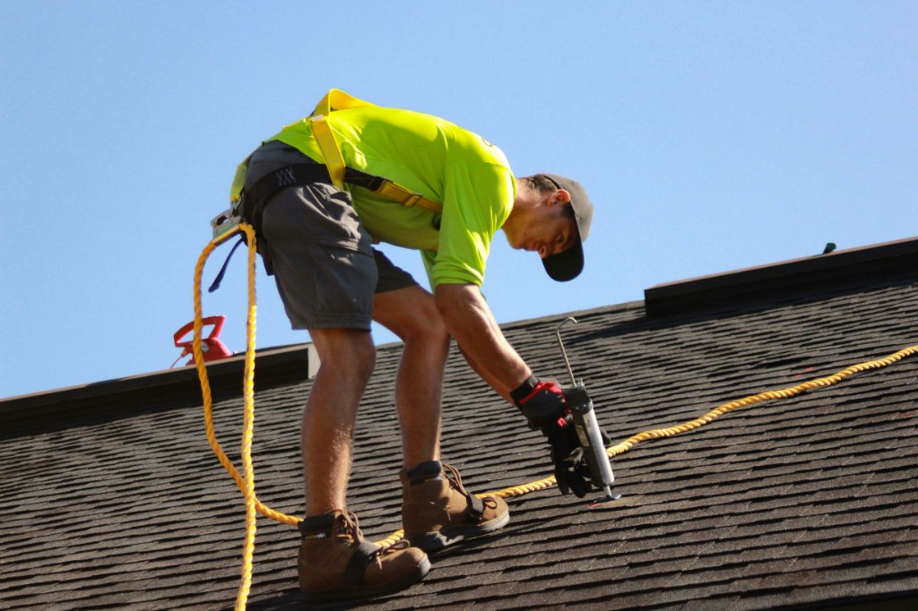A roofer in high-visibility gear working on a shingle roof